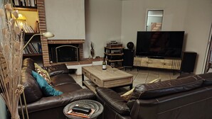 Uma sala de estar moderna com um sofá de couro, uma mesa de centro, lareira, televisão de tela plana e estante de livros.