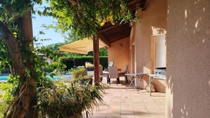 Uma área de varanda coberta com piscina, mobiliário externo e uma pérgula para proteção do sol.