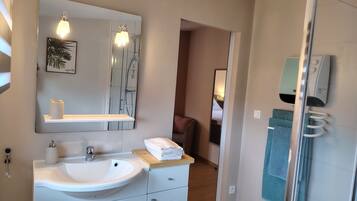 A modern bathroom with a large mirror, a sink, and a shower area.