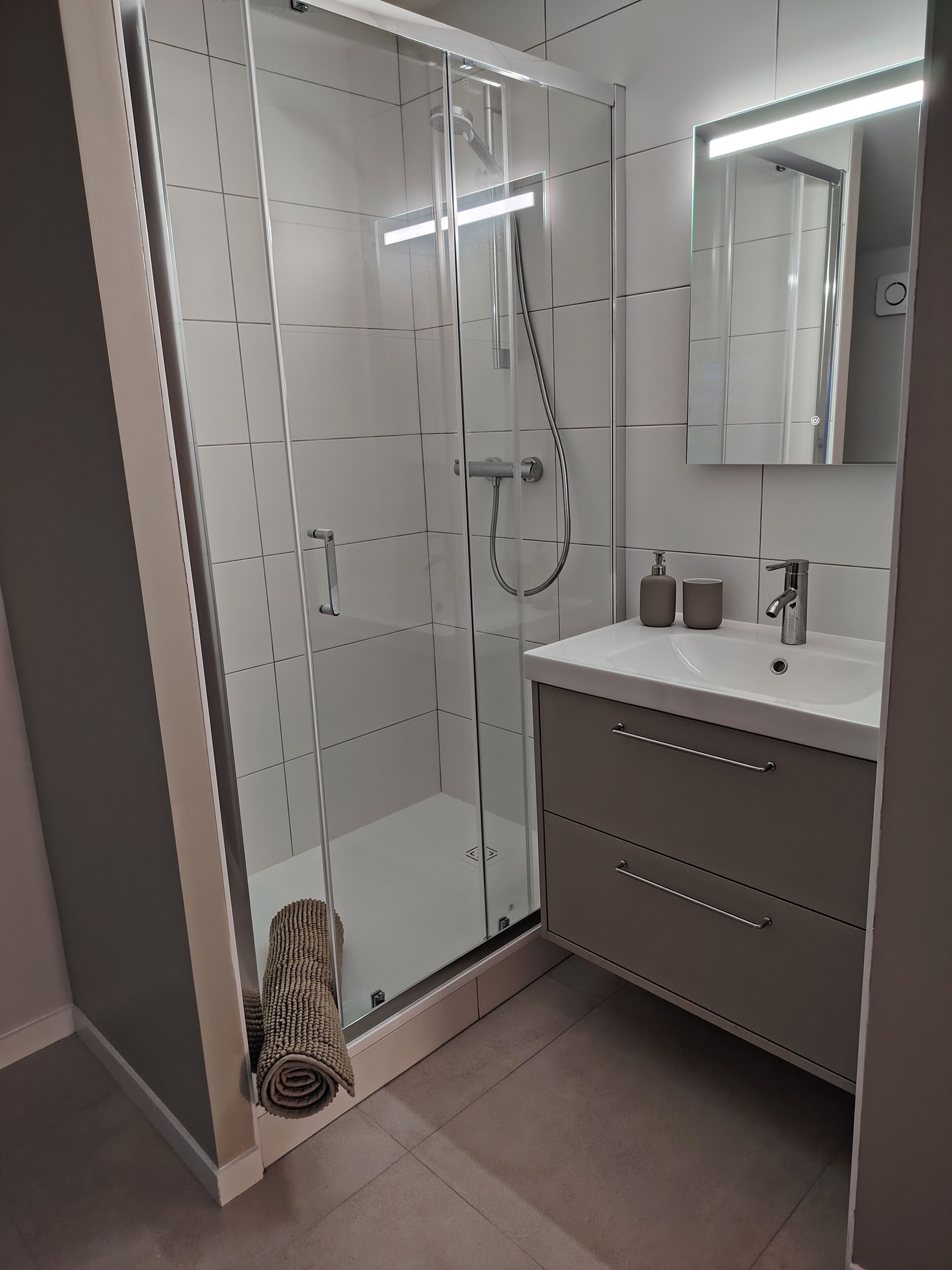 A modern bathroom with a glass-enclosed shower, a white sink, and a mirror above the vanity.