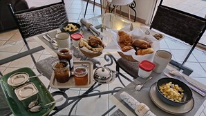Uma mesa de vidro com disposição para o café da manhã, incluindo pães, frutas e acompanhamentos.