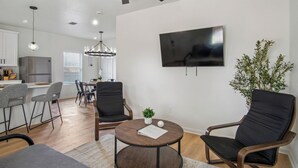A modern living room with a round coffee table, two black armchairs, a TV mounted on the wall, and a dining area in the background. - Your Inner-City Sanctuary: 3BR/2BA Near Riverwalk (San Antonio)