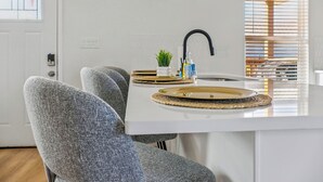 A modern kitchen with a white countertop, a black faucet, and a pendant light. There are two grey upholstered chairs and a small potted plant on the counter. - Your Inner-City Sanctuary: 3BR/2BA Near Riverwalk (San Antonio)