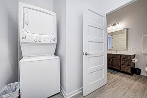 A laundry room with a front-loading washer and dryer, a bathroom with a sink and mirror, and a door leading to another room. - Fishers - King bed - First Level (Fishers)