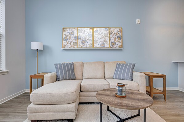 A living room with a sectional sofa, a round coffee table, and a decorative wall piece. - Fishers - King bed - First Level (Fishers)