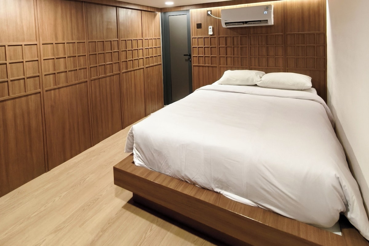 Una camera da letto con un letto, pannelli in legno, un condizionatore d'aria e una luce a soffitto incassata.