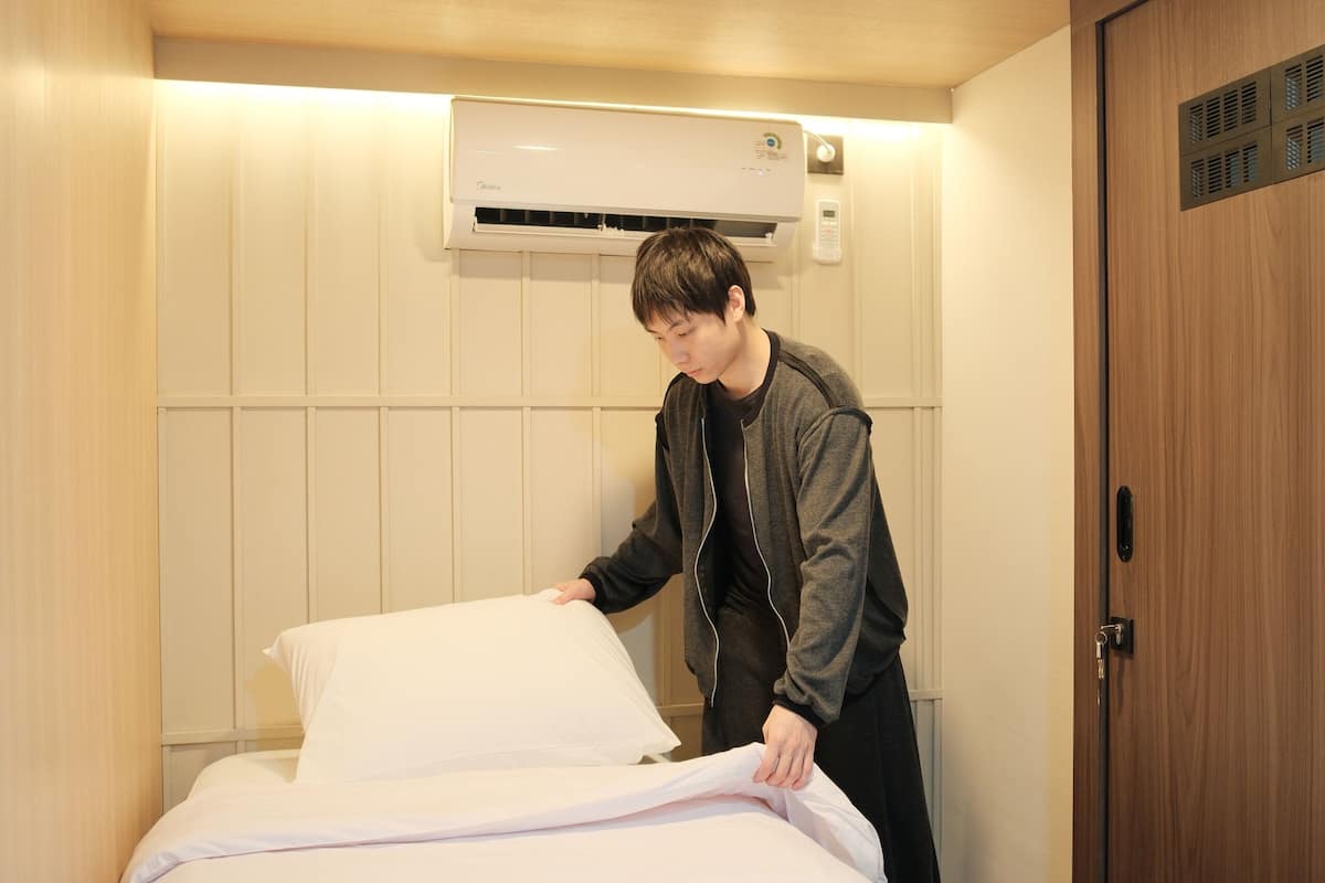 A hotel room with a bed, a wooden door, and an air conditioning unit on the wall.