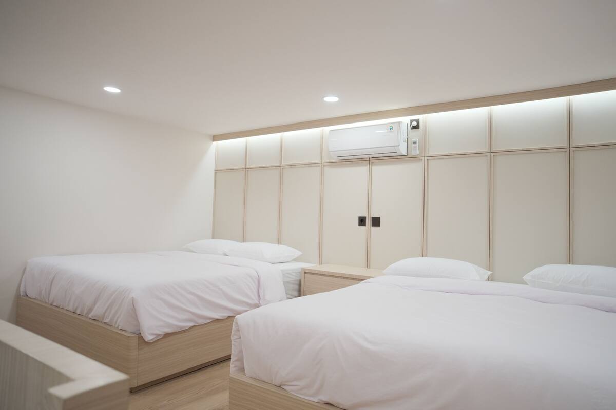 A modern bedroom with two single beds, a built-in air conditioning unit, and a minimalist design.