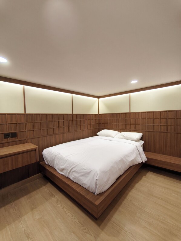 A modern bedroom with a wooden headboard, a wooden bedside table, and a large bed with white bedding. - INSAHAUS Guest House Malang (Malang)