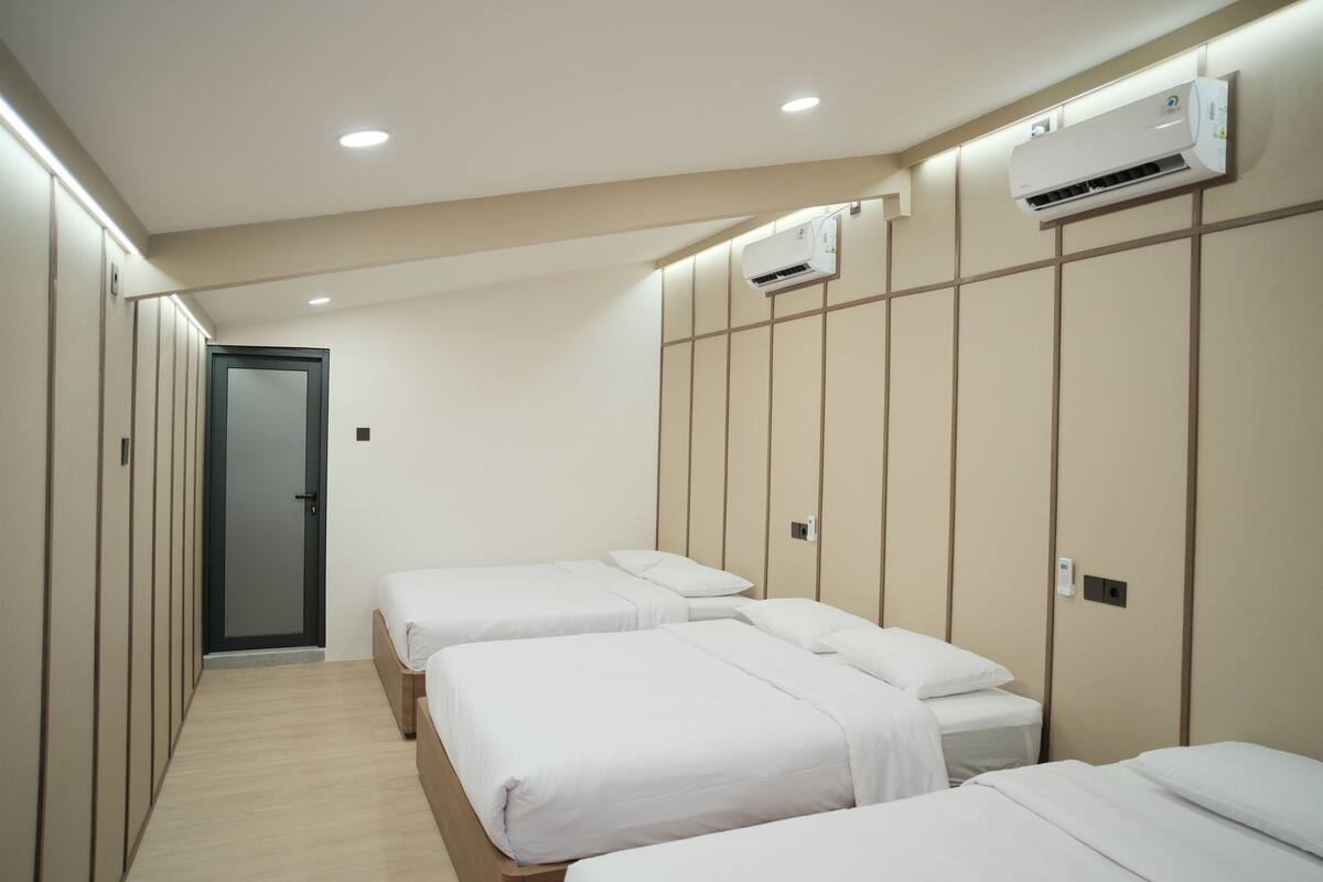 A hotel room with three beds, a wardrobe, and an air conditioning unit.