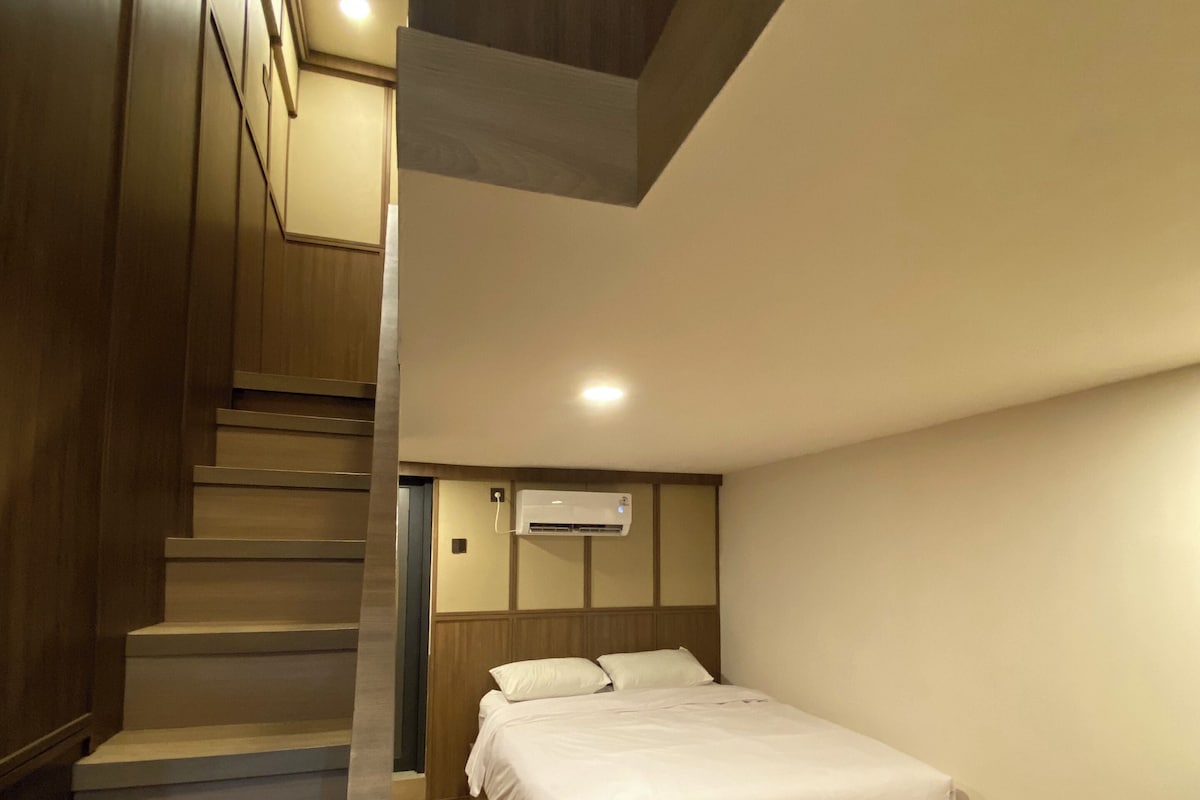 Una camera da letto con un letto, pavimento in legno, una scala e un condizionatore d'aria.