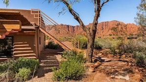 A desert landscape with a building featuring a wooden staircase and a view of red rock formations. - 2 bed 2 bath in the Kayenta Art Village W/Views of the red rock cliffs. (Ivins)