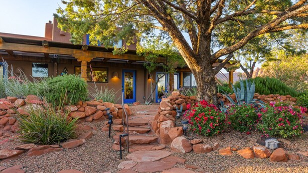 A house with a stone pathway leading to the entrance, surrounded by various plants and rocks. - 2 bed 2 bath in the Kayenta Art Village W/Views of the red rock cliffs. (Ivins)