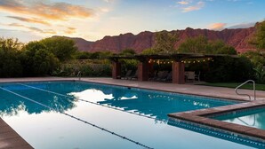 A swimming pool with clear water, lounge chairs, and a pergola with string lights. - 2 bed 2 bath in the Kayenta Art Village W/Views of the red rock cliffs. (Ivins)