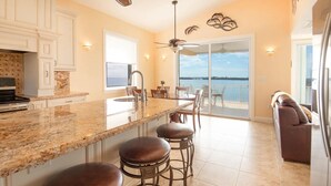 Una cocina amplia con una isla grande, taburetes de bar y vista al océano a través de un ventanal corredero.