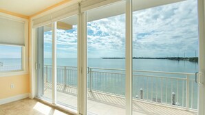 Una habitación con grandes puertas correderas de vidrio que dan a un balcón con vista al mar y una isla distante.