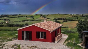 Een rood gebouw met een pannendak, omringd door een grindpad, gelegen voor een achtergrond van glooiende groene heuvels en een regenboog.