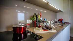 Een moderne keuken met een roestvrijstalen afzuigkap, een rode pan op een inductiekookplaat, een snijplank met groenten, en een spoelbak met een kraan.