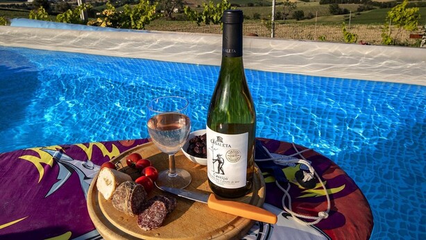 Een zwembadterras met een fles Castiglio wijn, een glas rosé en een houten plank met plakjes salami en brood.