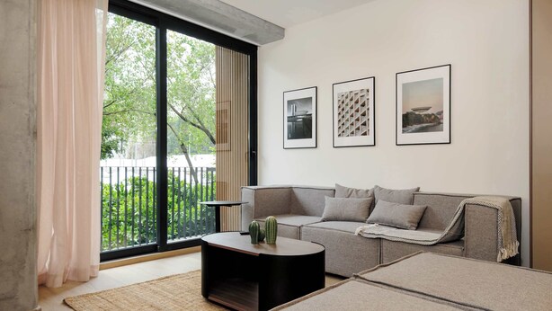 A modern living room with a sofa, a coffee table, and a large window with a view of greenery. There are three framed pictures on the wall. - w* | Sophisticated 3BR in the Heart of Cuauhtemoc (Ciudad de México)
