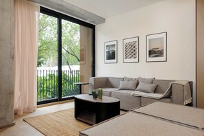 A modern living room with a sofa, a coffee table, and a large window with a view of greenery. There are three framed pictures on the wall. - w* | Sophisticated 3BR in Cuauhtemoc w/ Pool (Ciudad de México)