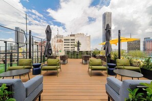 An outdoor seating area with green chairs and tables, umbrellas, and a view of city buildings. - w* | Sophisticated 3BR in Cuauhtemoc w/ Pool (Ciudad de México)