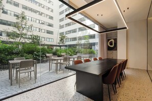 Una sala de conferencias moderna con una gran mesa y sillas, ventanas amplias y vistas a un edificio y follaje exterior.