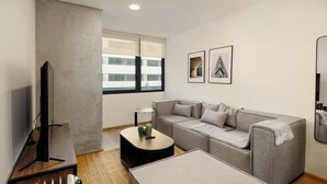 Ett modernt vardagsrum med en grå soffa, ett soffbord, en tv och ett element.
