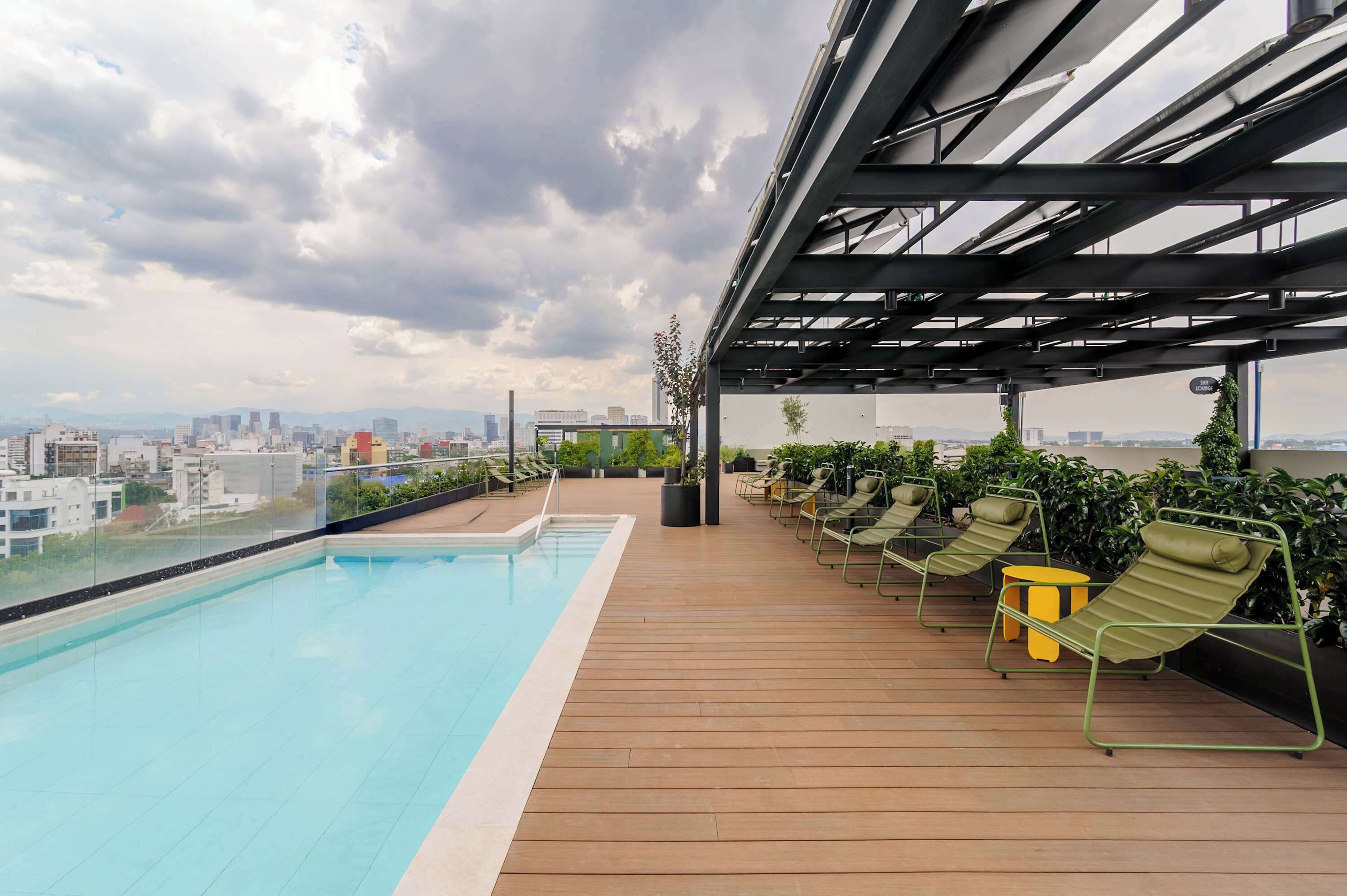 A rooftop pool area with a city view, lounge chairs, and a pergola structure.