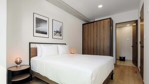 Ein modernes Schlafzimmer mit einem großen Bett, einem Holzkopfstück, zwei gerahmten Bildern an der Wand, einem Nachttisch mit Lampe und einem Holzschrank.