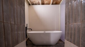 Een moderne badkamer met een vrijstaand bad, betegelde wanden en een zichtbare douchehoek.
