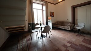 Een woonkamer met een bank, een eettafel met stoelen, een klein keukentje en een deur.