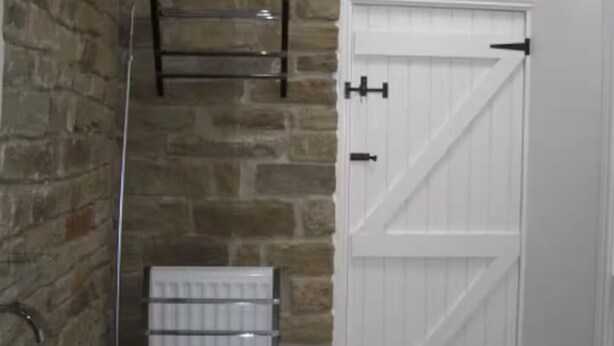 Une salle de bain avec un mur en pierre, une porte blanche et un lavabo blanc.