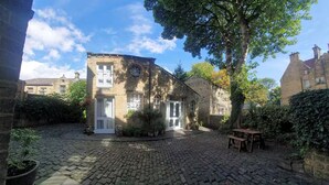 Une cour dallée de pierres, un banc en bois et un bâtiment doté d’une fenêtre ronde et de portes blanches.