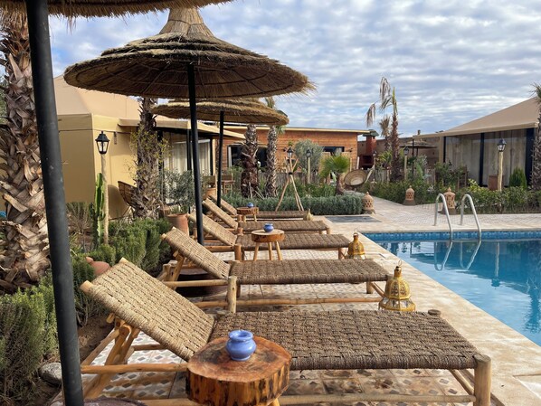 A poolside area with lounge chairs, a thatched umbrella, and a pool.