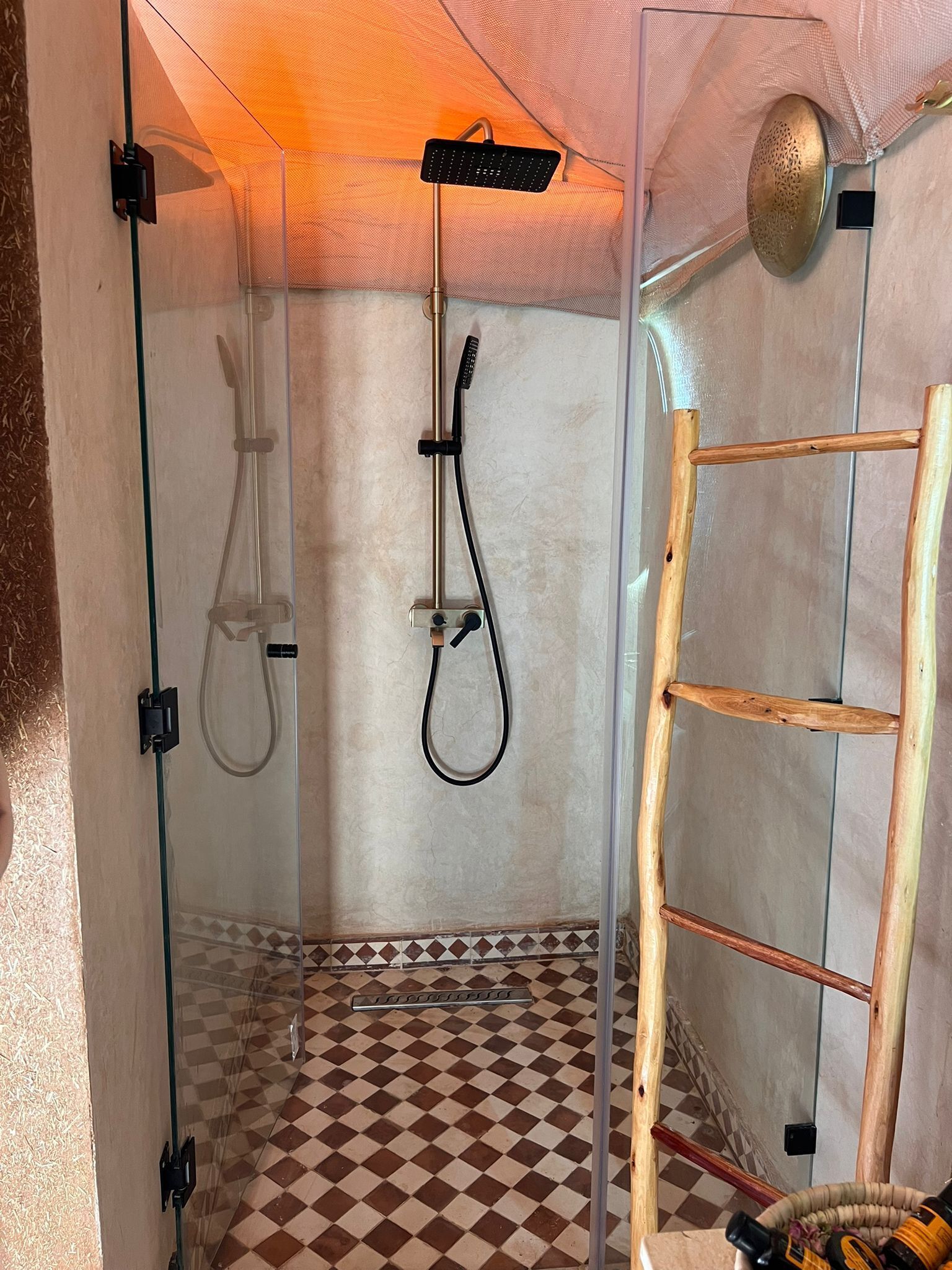 Un espace de douche clos par des parois de verre, doté d’un sol à carreaux, d’une échelle en bois et d’un pommeau de douche.