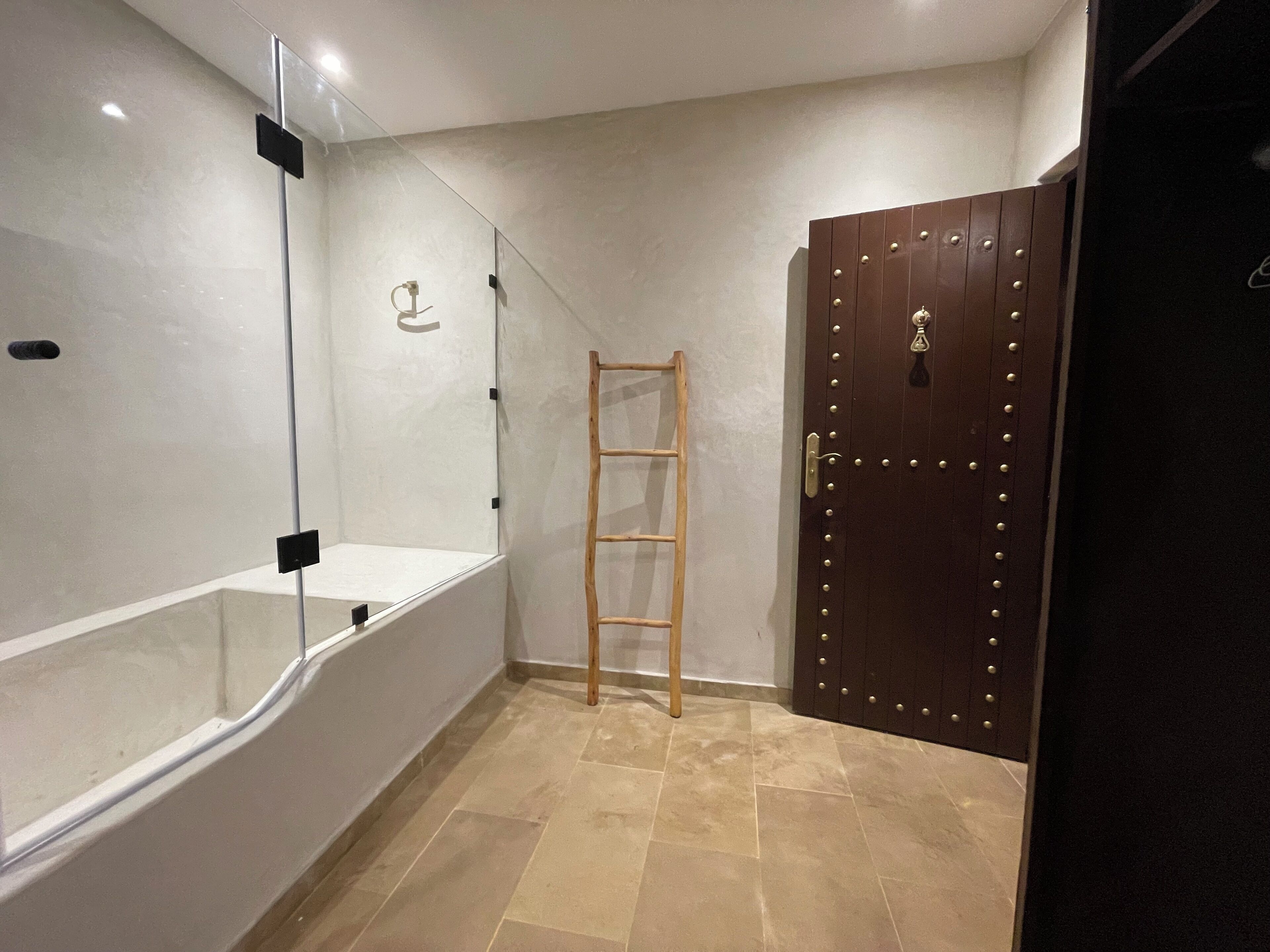 Un baño con cabina de ducha de vidrio, una escalera de madera y una puerta de madera oscura con tiradores de latón.