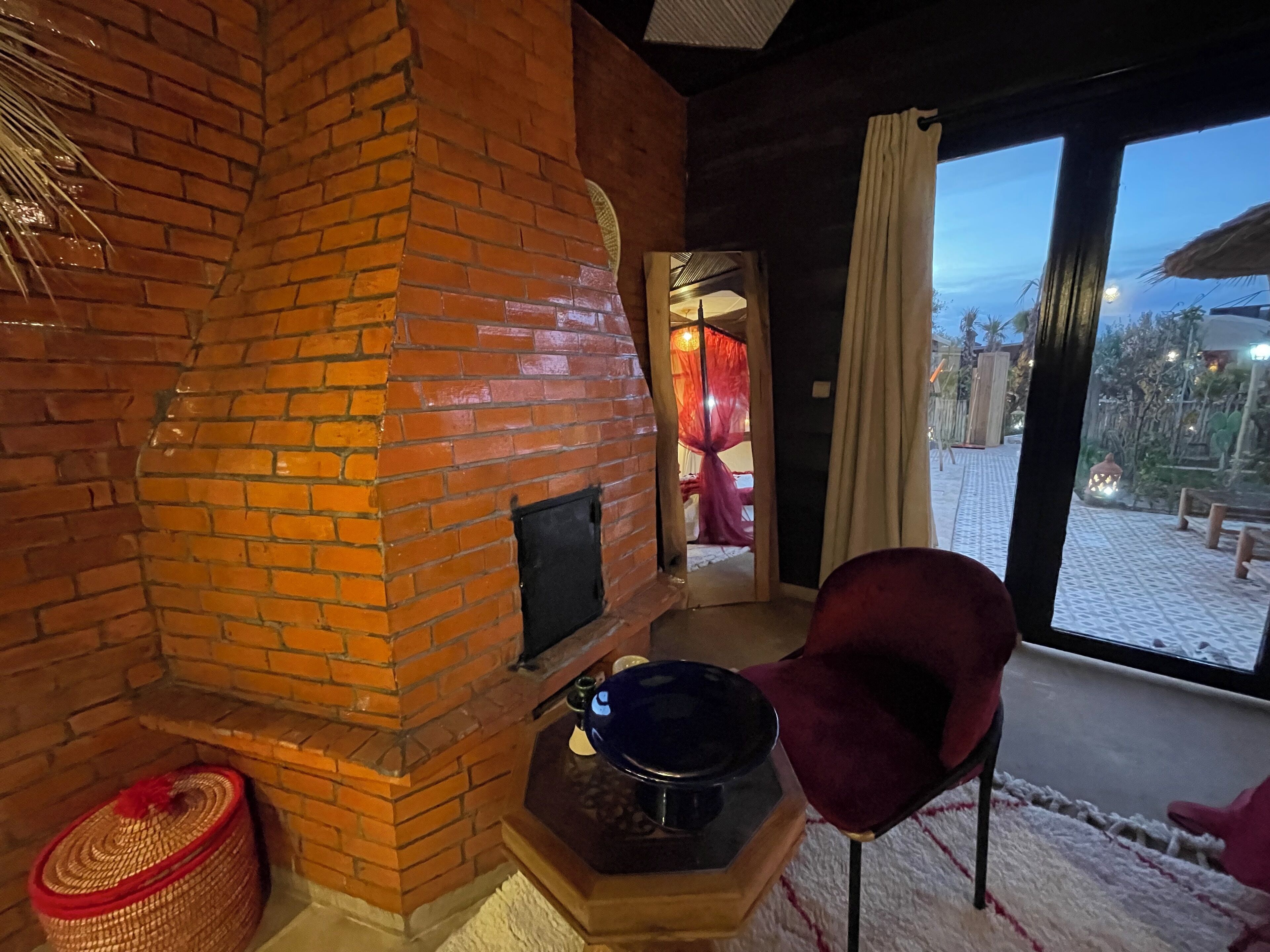 Um quarto aconchegante com lareira de tijolos, uma poltrona confortável e vista para área externa coberta de neve.
