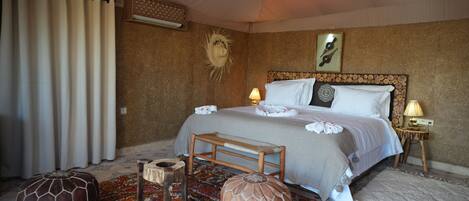Een slaapkamer met een bed, bedlampen, een houten hoofdbord, een kamerbreed tapijt met een patroon en twee poefs.