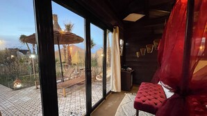 A room with large windows, a red chair, a small table, and a patterned rug.