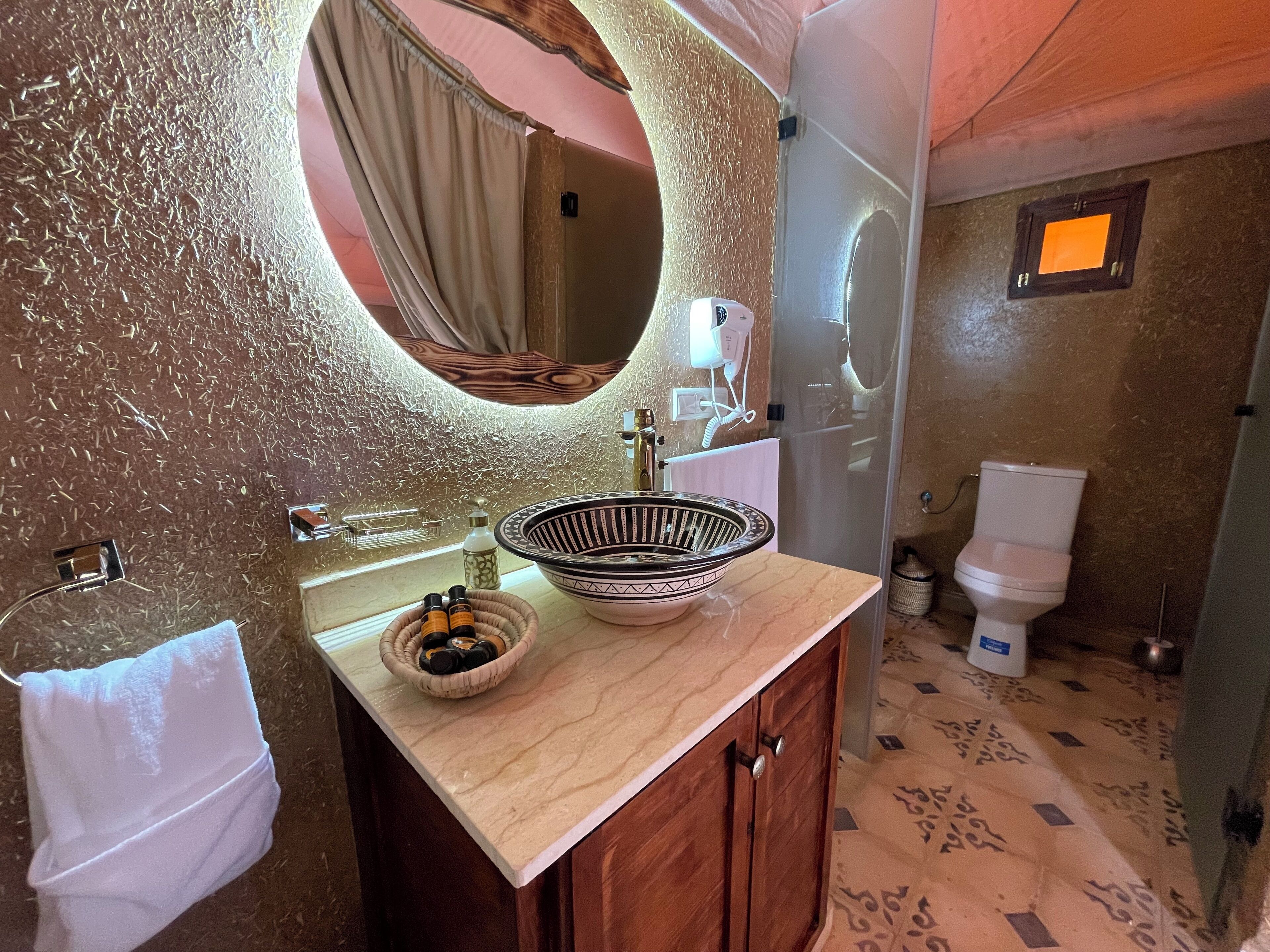 A bathroom with a round mirror, a sink with a bowl, a towel, and a toilet.