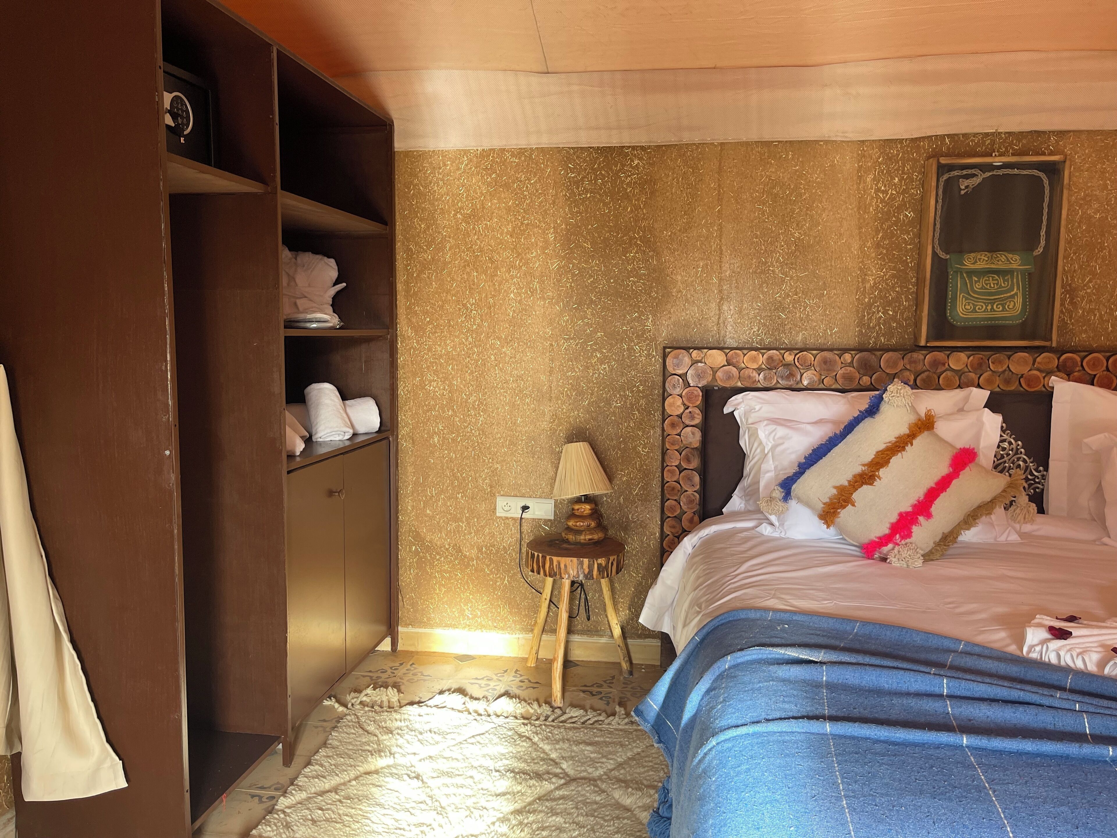 Una habitación de hotel con cama, armario de madera, una mesita con lámpara y un adorno en la pared.