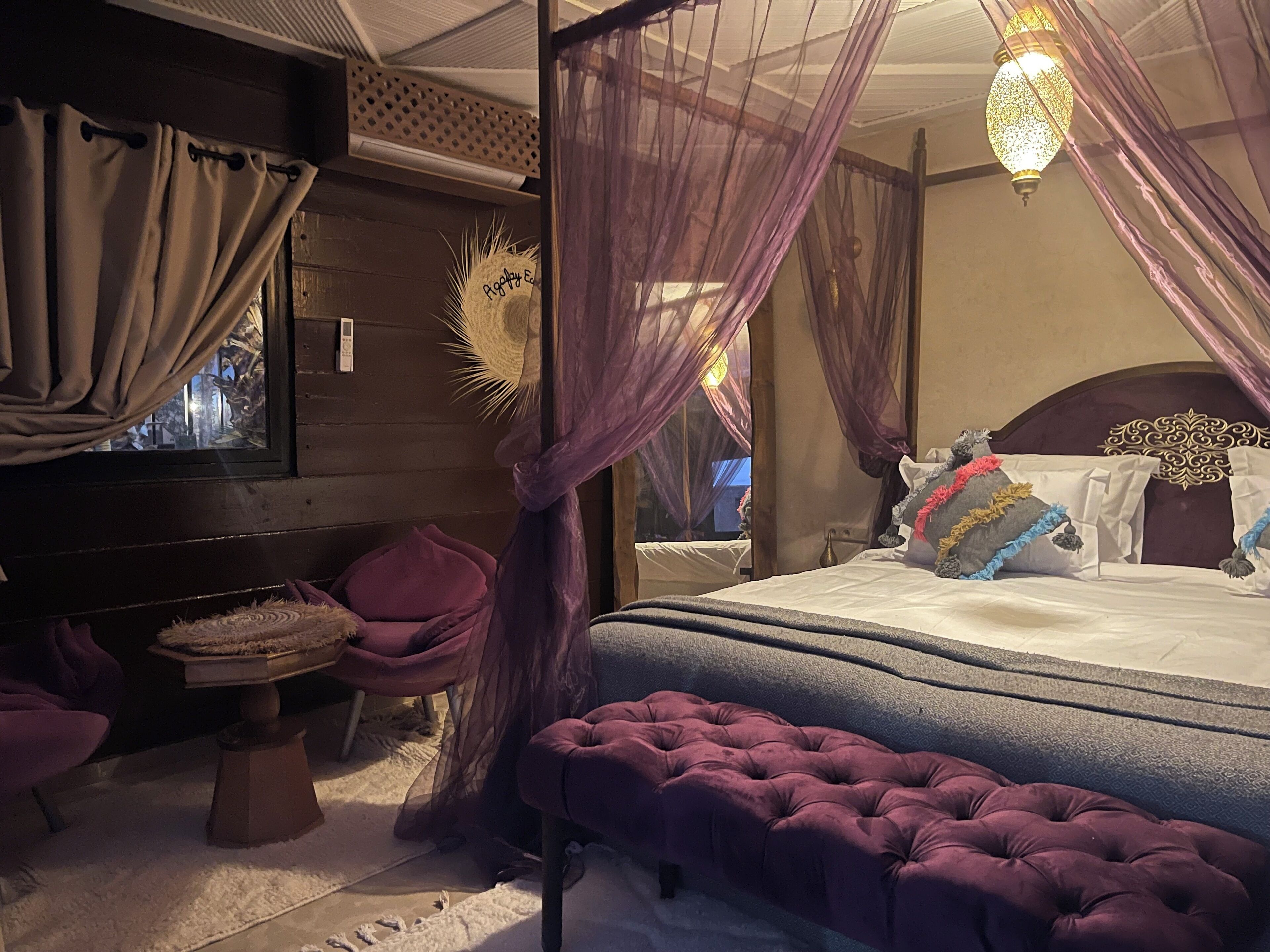 A room with a bed, a bench, and a window with curtains.