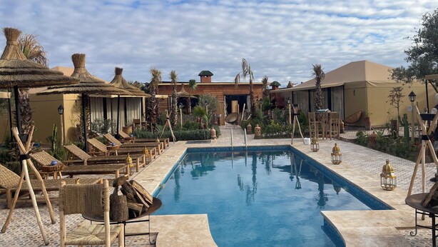 A pool area with lounge chairs, thatched umbrellas, and a wooden deck.