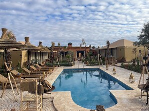 A pool area with lounge chairs, thatched umbrellas, and a wooden deck.