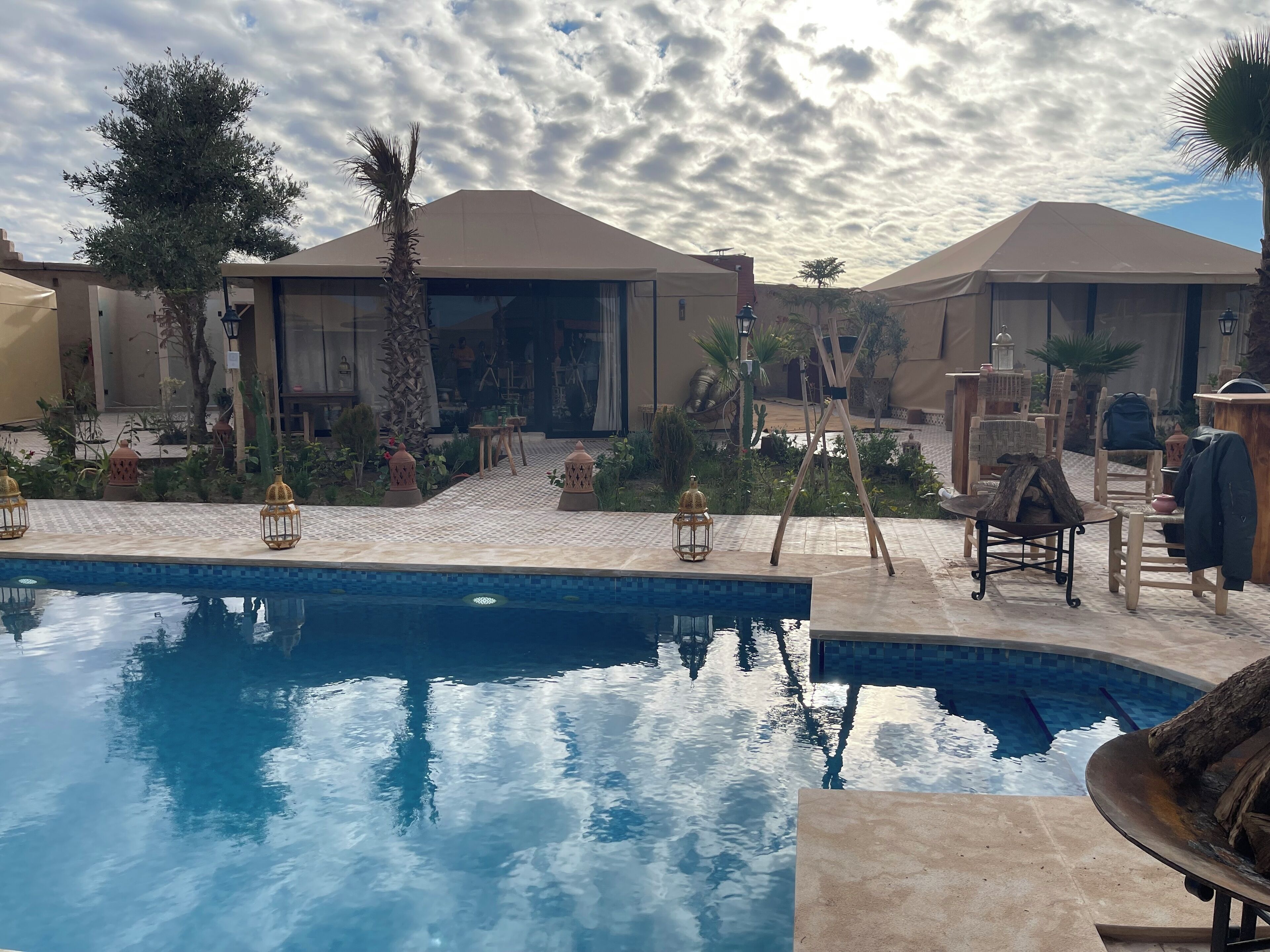 A pool area with a tiled deck, palm trees, and outdoor furniture.