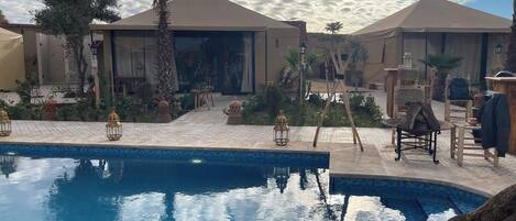 A pool area with a tiled deck, palm trees, and outdoor furniture.