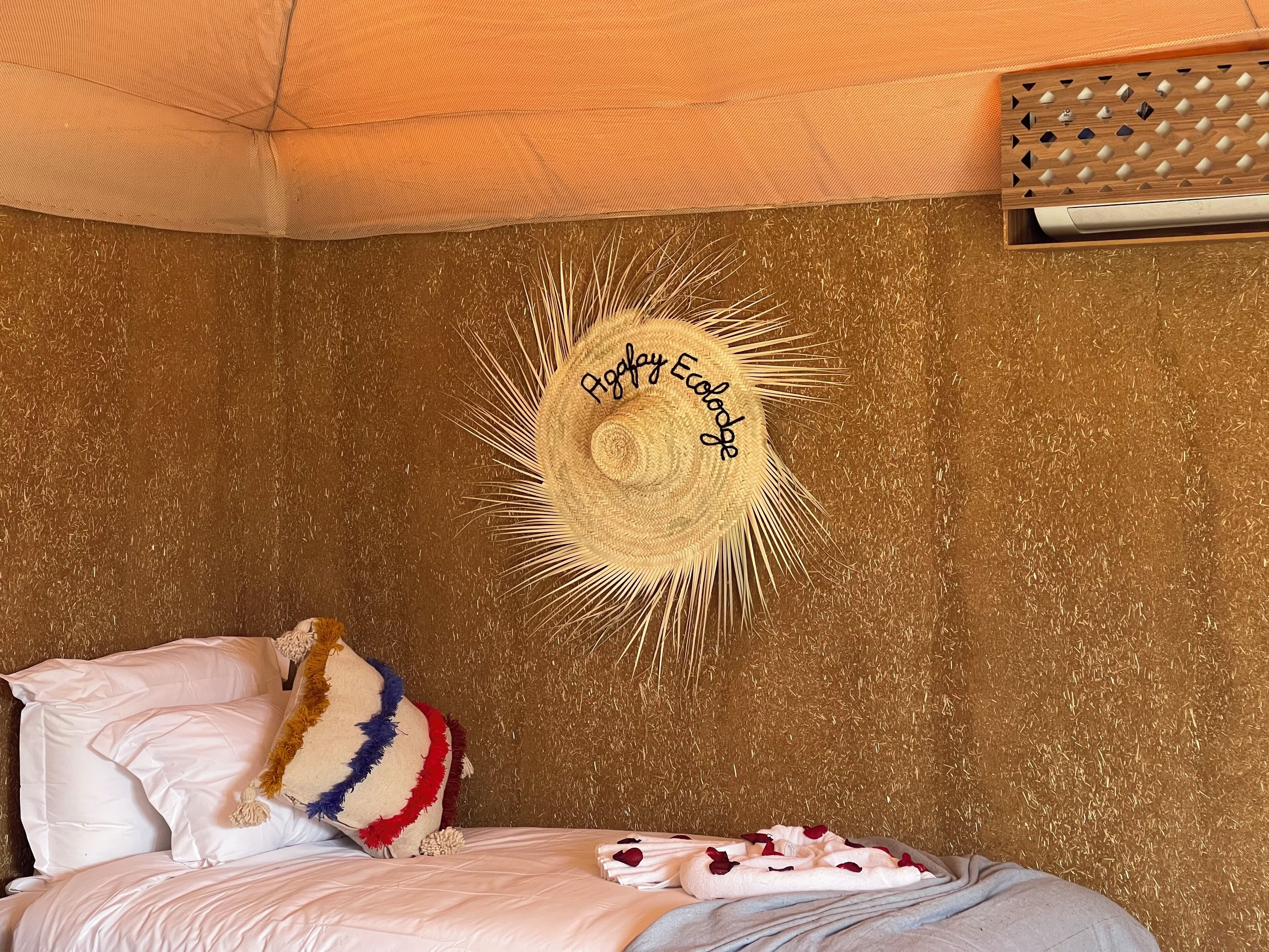 A cozy room with a bed, a decorative sun hat on the wall, and a textured wall.
