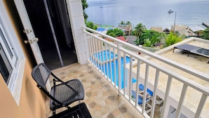 A balcony with a view of the sea, a pool, and a chair. - Stunning Ocean, City & Pool View 2 Bedroom Apt. 2 minutes from Roseau (Roseau)