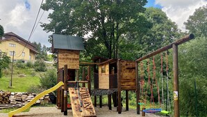 Une structure de jeu en bois comprenant un toboggan, un filet d’escalade et des ponts de corde.